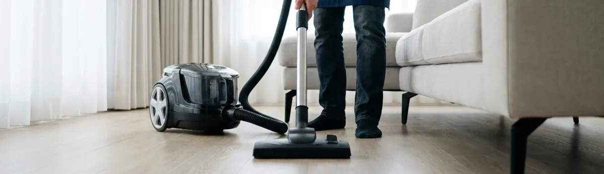 Professional house cleaner vacuuming a living room floor with a canister vacuum cleaner, Columbia, MO.